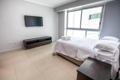 een witte slaapkamer met een bed en een televisie bij Suite Vista al río con Balcón en puerto Santa Ana in Guayaquil