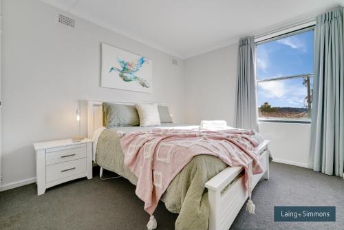 a white bedroom with a bed and a window at TC GARDENS 12 in Armidale