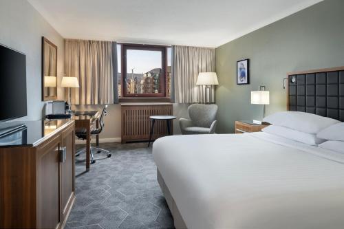 スウォンジーにあるDelta Hotels by Marriott Swanseaのベッド、デスク、テレビが備わるホテルルームです。