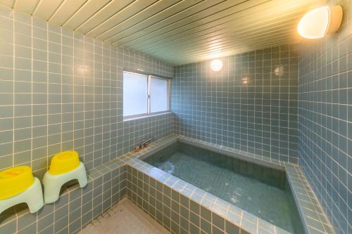 un bagno con piastrelle blu, vasca e 2 sgabelli. di Fujiyoshi a Nozawa Onsen