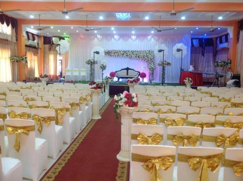 a banquet hall with white chairs and gold bows at Hotel Juli Reception in Mannar