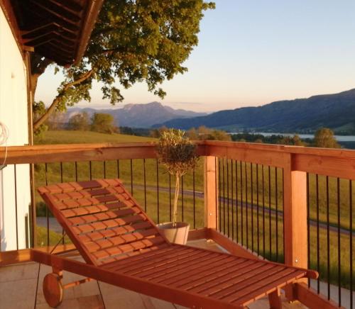 a wooden bench on a deck with a view of the mountains at Roiderhof Irrsee in Oberhofen am Irrsee