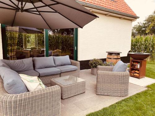 a patio with wicker furniture and an umbrella at Prachtige vakantiewoning met weids uitzicht in Maldegem