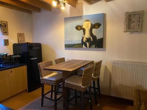 a dining room table with chairs and a painting of a cow at Prachtige vakantiewoning met weids uitzicht in Maldegem