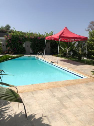 uma grande piscina com um guarda-sol vermelho em Villa magnifique avec piscine em Somone