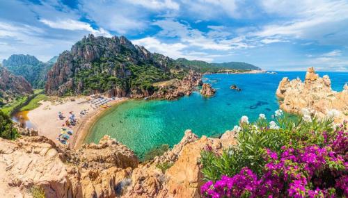 a beach with people in the water and rocks at Casa Smeralda - Piscina e vista sul Mare! in Trinità dʼAgultu