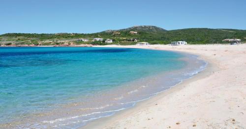 a beach with blue water and houses in the background at Casa Smeralda - Piscina e vista sul Mare! in Trinità dʼAgultu