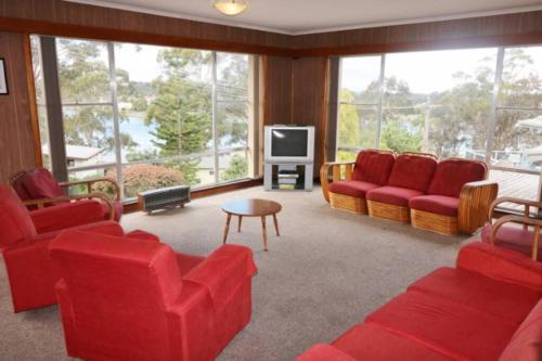 a living room with red chairs and a tv at Osborne House - 4 Bedroom in Merimbula