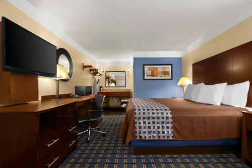 a hotel room with a bed with a desk and a flat screen tv at Days Inn by Wyndham Fultondale in Fultondale
