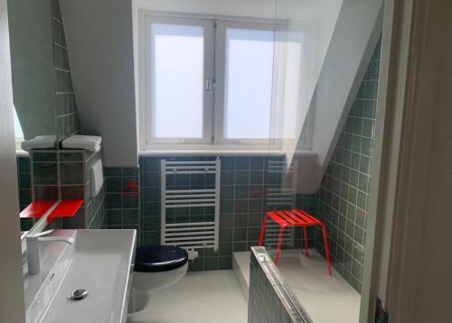 een groene betegelde badkamer met een raam en een rode kruk bij The Great Hideaway in Vreeland