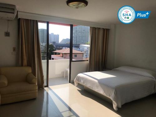 a bedroom with a bed and a chair and a window at Jomtien Longstay Hotel - SHA Plus Certified in Jomtien Beach