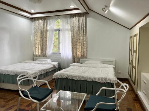 two beds in a room with a glass table and chairs at CAMPJOHNHAY Forest Estate in Baguio