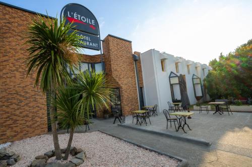 a building with tables and chairs and a palm tree at Hôtel L'Etoile Aéroport - A61 in Carcassonne