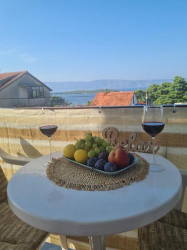a plate of fruit on a table with two glasses of wine at Bura in Jelsa