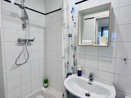 La salle de bains blanche est pourvue d'un lavabo et d'une douche. dans l'établissement LES MARAICHERS, à Strasbourg
