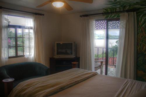 a bedroom with a bed and a tv and windows at Gingerbread Restaurant & Hotel in Nuevo Arenal