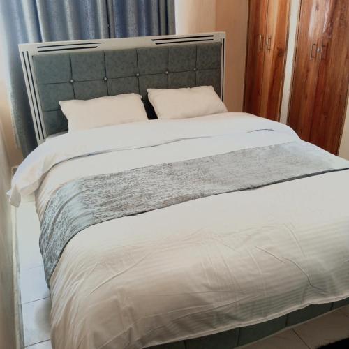 a bed with a gray headboard and white sheets and pillows at Milly's homes in Kakamega