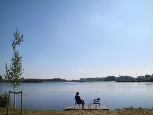 a man sitting on a dock in front of a lake at Lakeview villa with swimming and fishing pier in Simonshaven