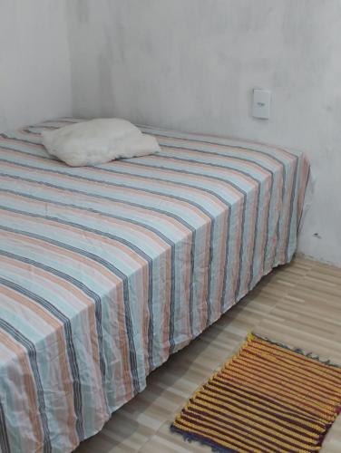 Una cama con una manta a rayas y una almohada. en Casa laranja cabuçu, en Saubara