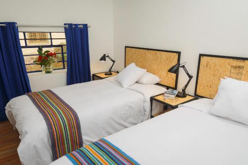 two beds in a room with blue curtains and two lamps at Saqray Hostel in Cusco