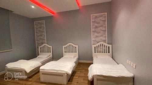 Cette chambre comprend trois lits et une lumière rouge. dans l'établissement شاليه العماريه, à Yanbu Al Bahr