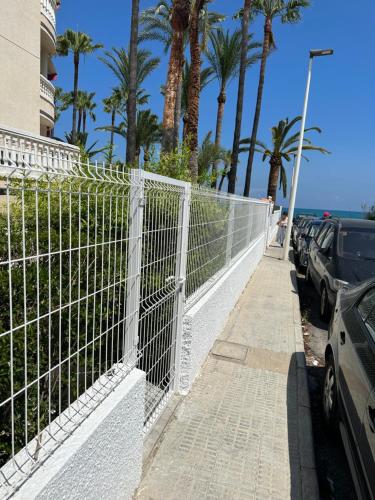 a white fence next to a parking lot with palm trees at Apartment Martinez Casablanca in Alcossebre