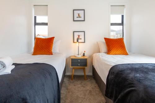 Duas camas com almofadas laranja num quarto em Art Deco 2 bed by Latimer Square em Christchurch