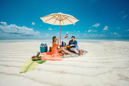 a man and woman sitting under an umbrella on the beach at Sun Siyam Olhuveli in South Male Atoll
