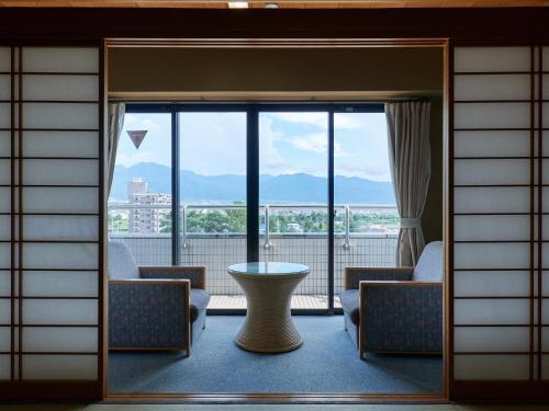 Tabist Onsen Hotel Toyo في Fuefuki: غرفة مع نافذة كبيرة مع طاولة وكراسي