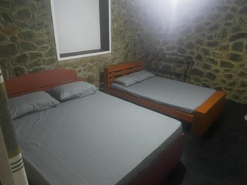 two twin beds in a room with a stone wall at Artomoro Ceylon motel in Demodera