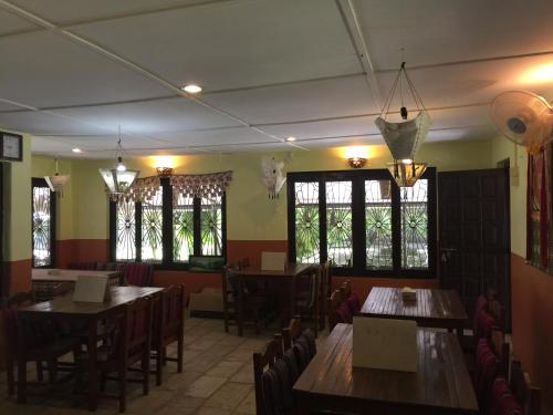 un restaurante con mesas y sillas de madera y ventanas en Chautari Garden Resort en Sauraha