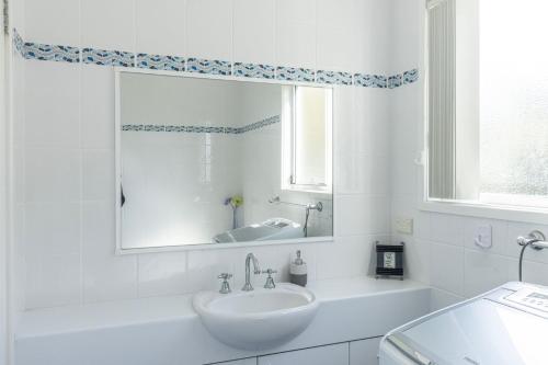 a white bathroom with a sink and a mirror at Coral Cottage in Berrara
