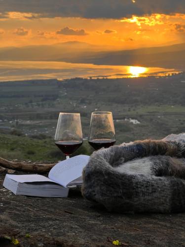 two glasses of wine and a book on a table with the sunset at green island in Ma'ale Gamla
