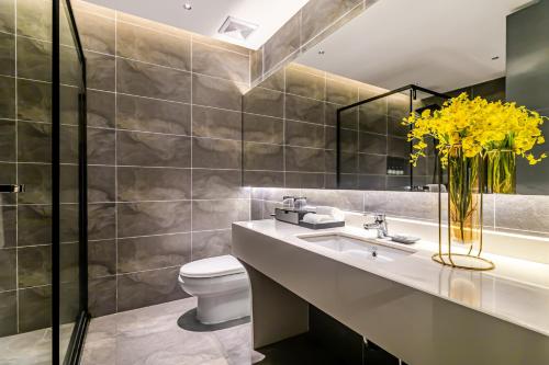 a bathroom with a sink and a toilet and a vase of yellow flowers at Empathy Hotel - Guangzhou East Railway Station Tianhe Sports Center in Guangzhou