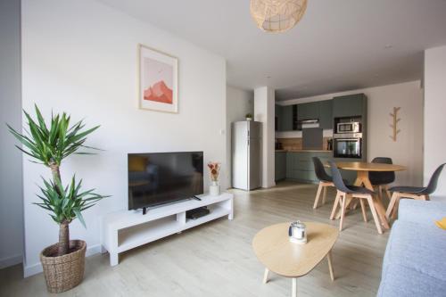 un salon avec une télévision, une table et des chaises dans l'établissement L'olivier - Appartement moderne et chaleureux - TRAM et PARC, à Grenoble