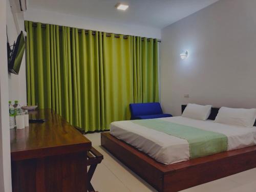 a bedroom with a bed and a desk and a green curtain at Hotel Serugahawatta in Wellawaya