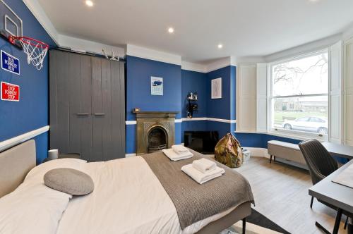 Stylish Family Home by Twickenham Stadium by UnderTheDoormat في لندن: غرفة نوم زرقاء مع سرير ومدفأة