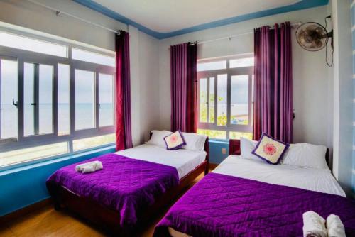 2 Betten in einem Zimmer mit lila Laken und Fenstern in der Unterkunft Thanh Tran Guesthouse Lý Sơn in Ly Son