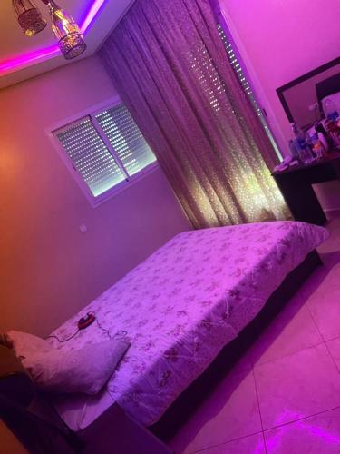 a purple bedroom with a bed with a window at Appartement meublé à neuf in Bouznika