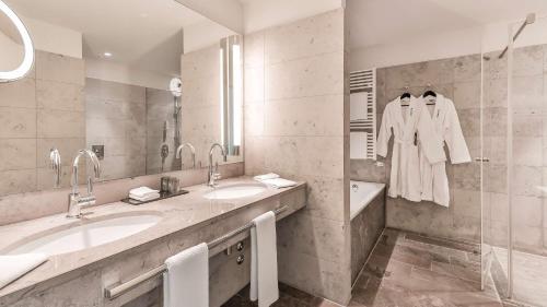 a bathroom with two sinks and a mirror and a tub at Dorint Hotel am Heumarkt Köln in Cologne