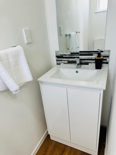 a white bathroom with a sink and a mirror at Spacious 4 bedroom House in Manukau in Auckland