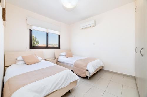 two beds in a room with white walls and a window at Blue Serenity Complex in Larnaca
