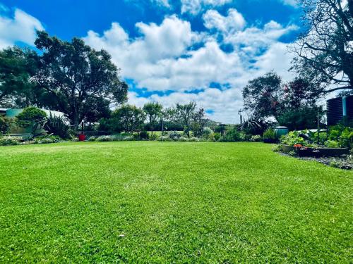 a large field of green grass with trees and clouds at Prom Beach House in Sandy Point