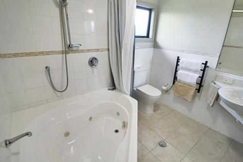 a bathroom with a tub and a toilet and a sink at Whangaparaoa Lodge in Whangaparaoa