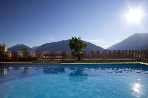 a swimming pool with a bench and mountains in the background at Hotel-Garni Appartement Gartenheim in Schenna