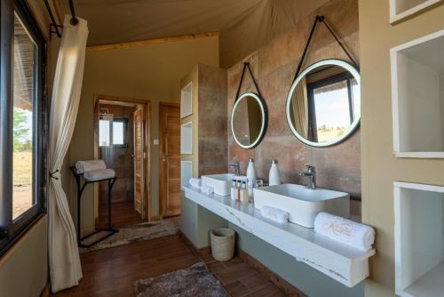 ein Badezimmer mit zwei Waschbecken und zwei Spiegeln in der Unterkunft Serengeti River Camp in Robanda