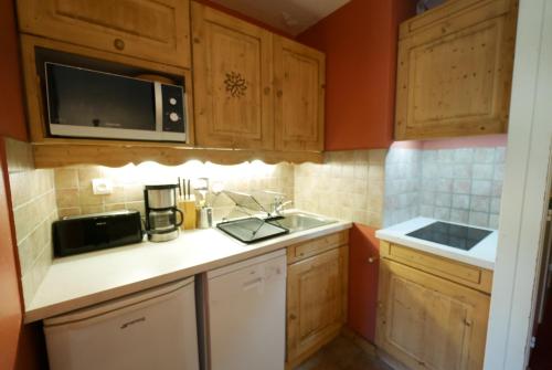 a kitchen with wooden cabinets and a sink and a microwave at Appartement les 2 alpes 1800 départ /retour skis aux pieds in Les Deux Alpes