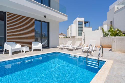 a swimming pool with white chairs next to a house at Villa Flora's 3-BR Retreat & Private Pool in Protaras in Paralimni