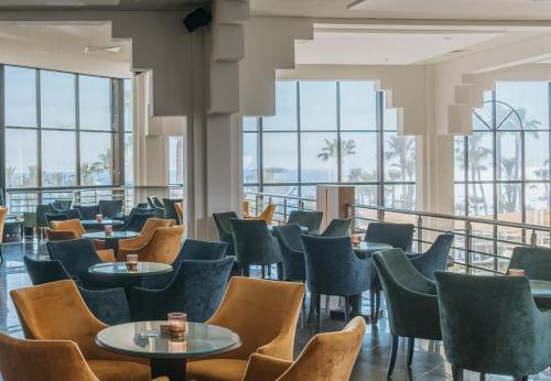 a restaurant with tables and chairs and windows at St George Beach Hotel & Spa Resort in Paphos