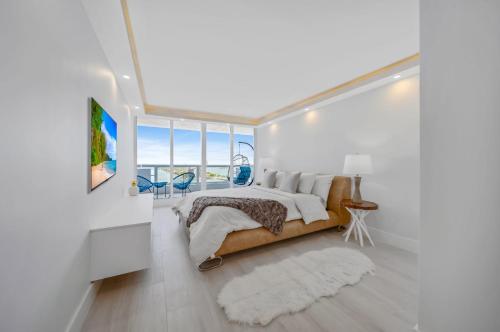a white bedroom with a bed and a balcony at Blooming Sun Direct Ocean View in Miami
